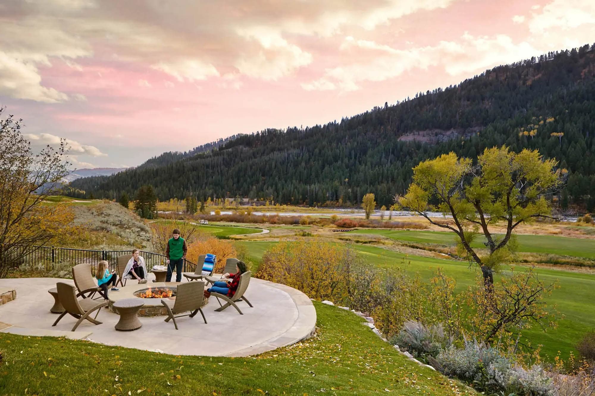 People gathered around a fire pit with mountains and the sunset in the background