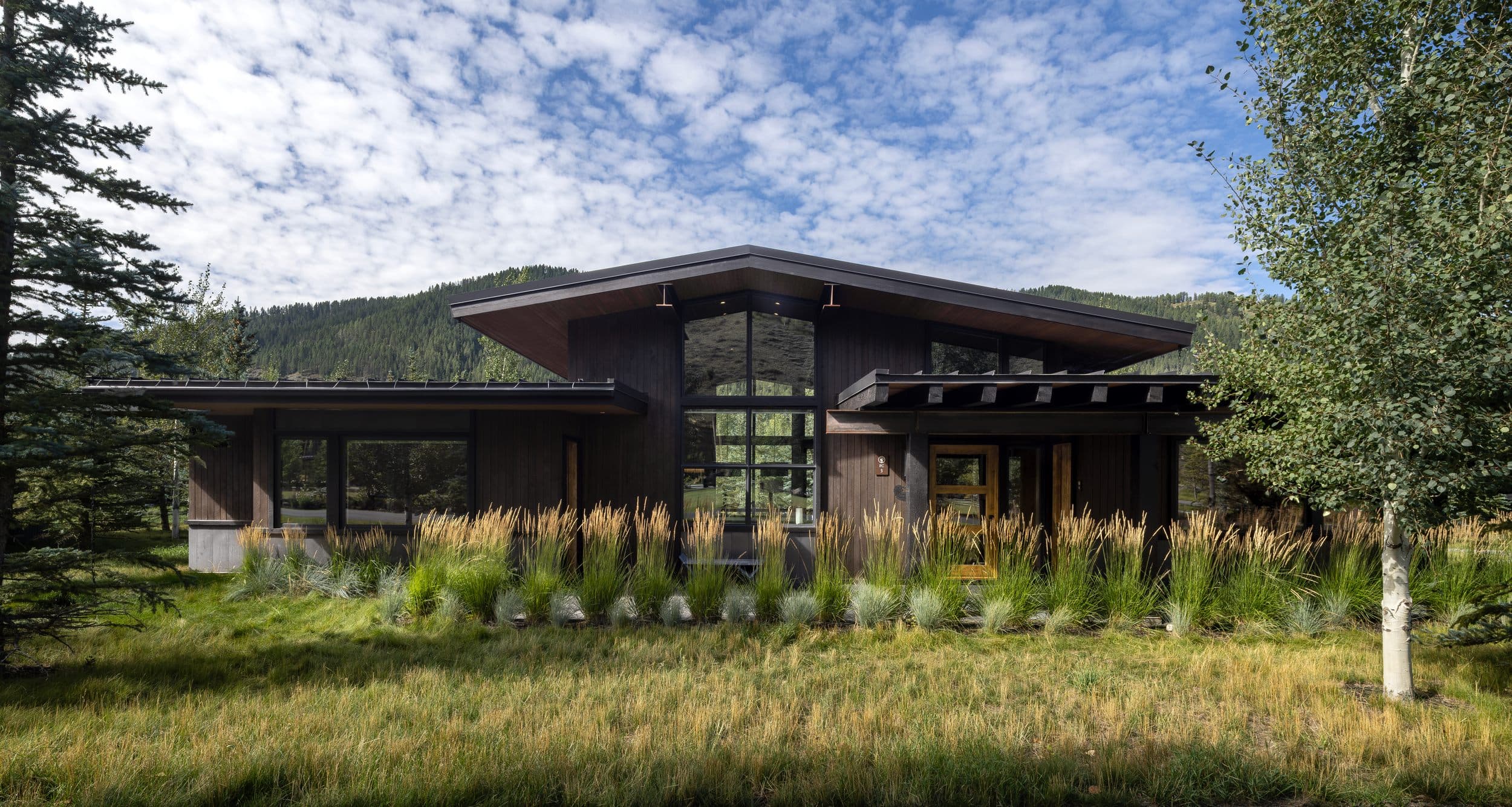 Luxury cabin exterior with floor-to-ceiling windows and native landscaping at Snake River Sporting Club in Jackson Hole