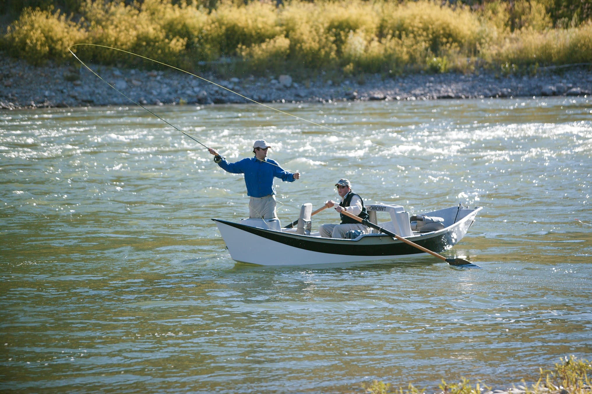 Angler casting from a drift boat with a guide on the Snake River near Snake River Sporting Club in Jackson Hole, Wyoming