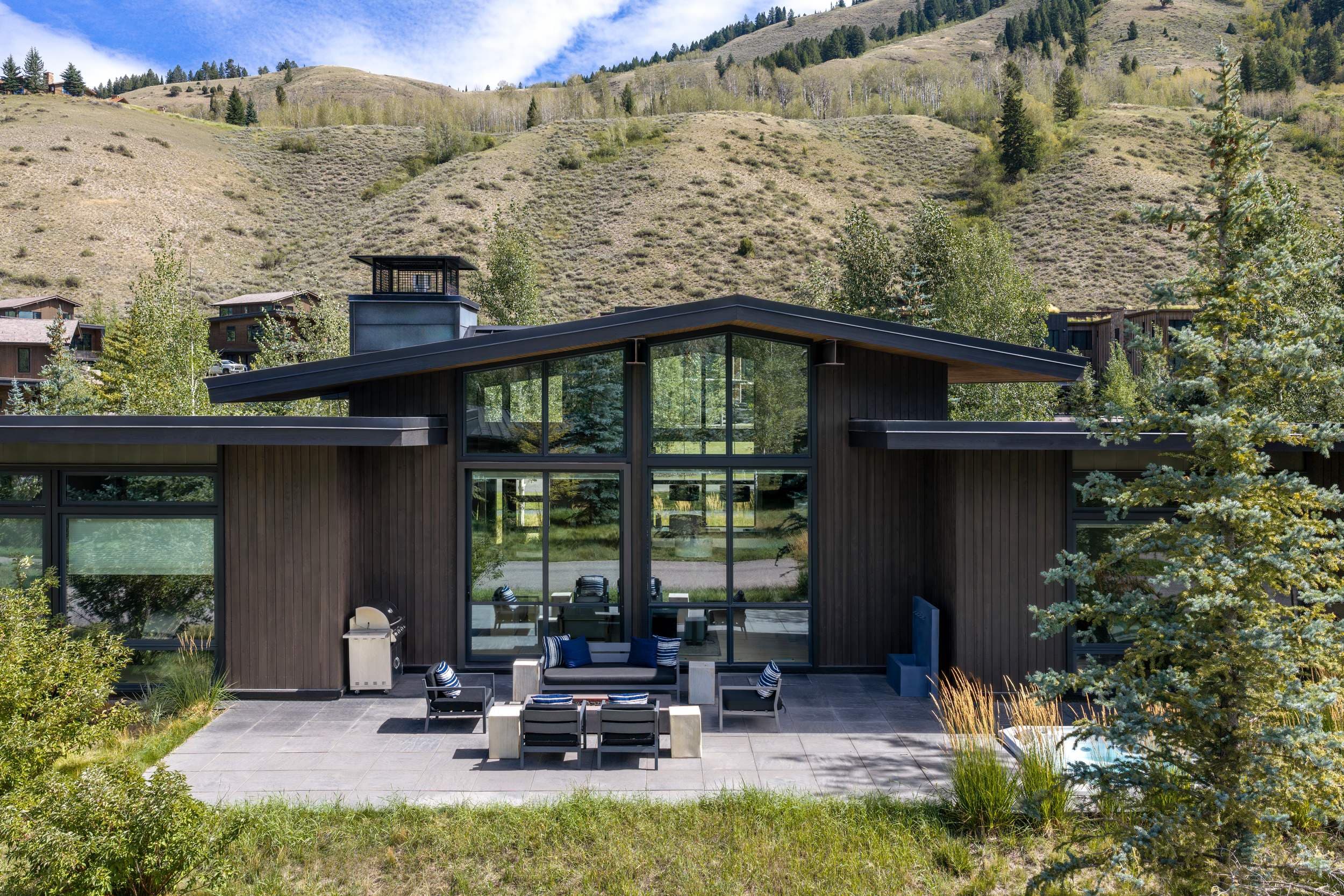 Aerial view of a modern mountain cabin with floor-to-ceiling windows and a stone patio at Snake River Sporting Club in Jackson Hole, Wyoming