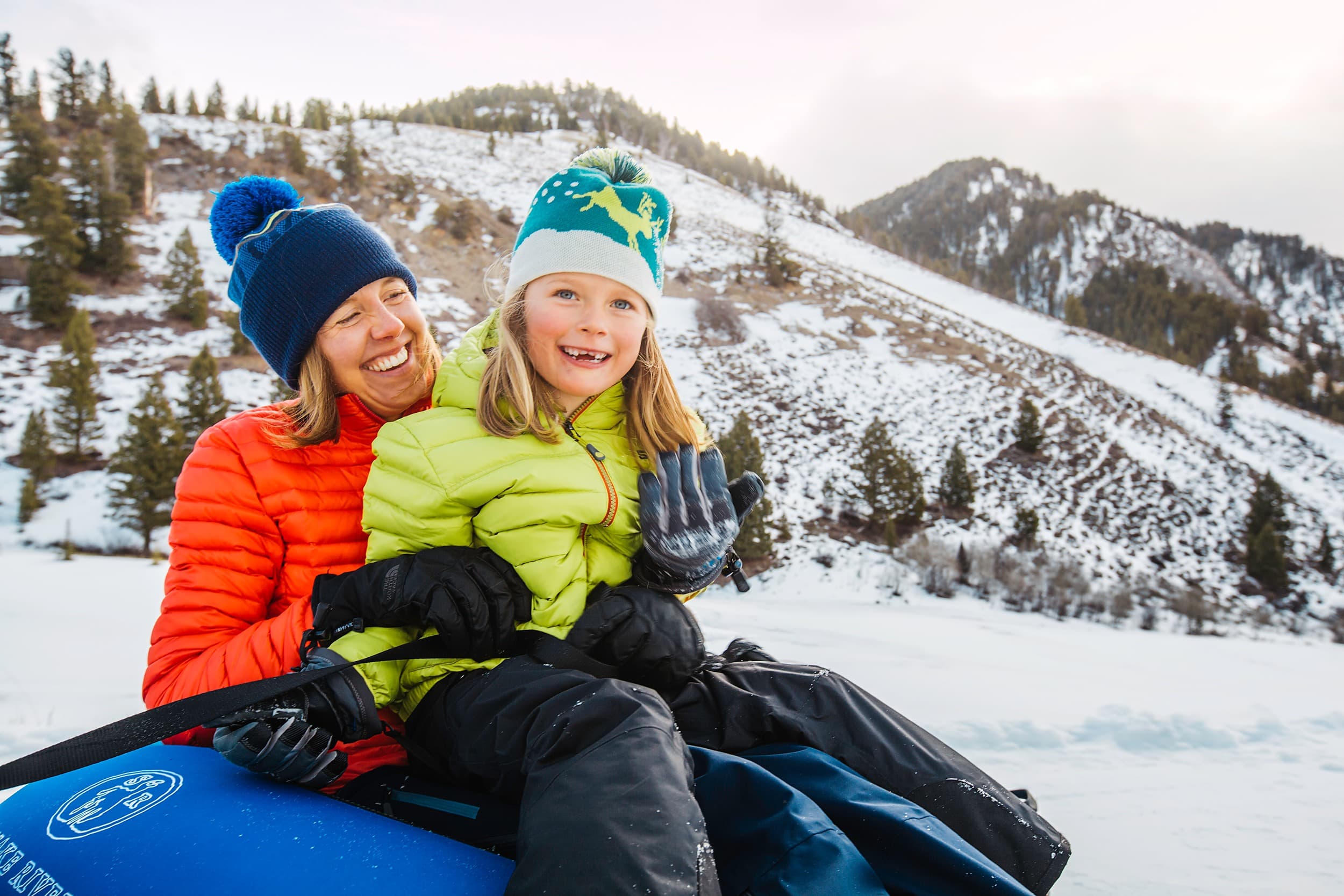 Mother and daughter smiling on a snow tube during winter activities at Snake River Sporting Club in Jackson Hole, Wyoming