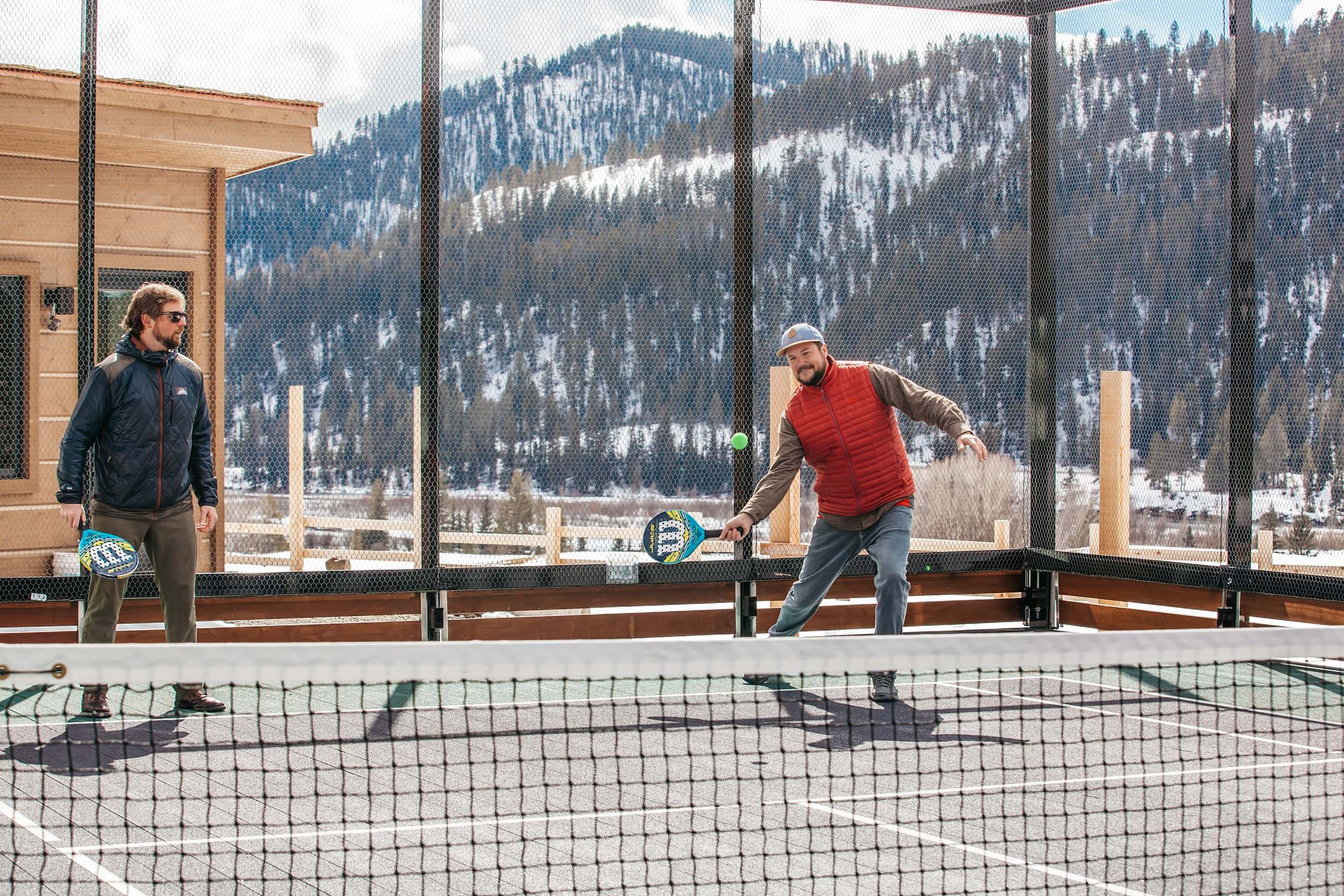 Two men playing paddle tennis on an outdoor court with snowy mountains at Snake River Sporting Club in Jackson Hole, Wyoming