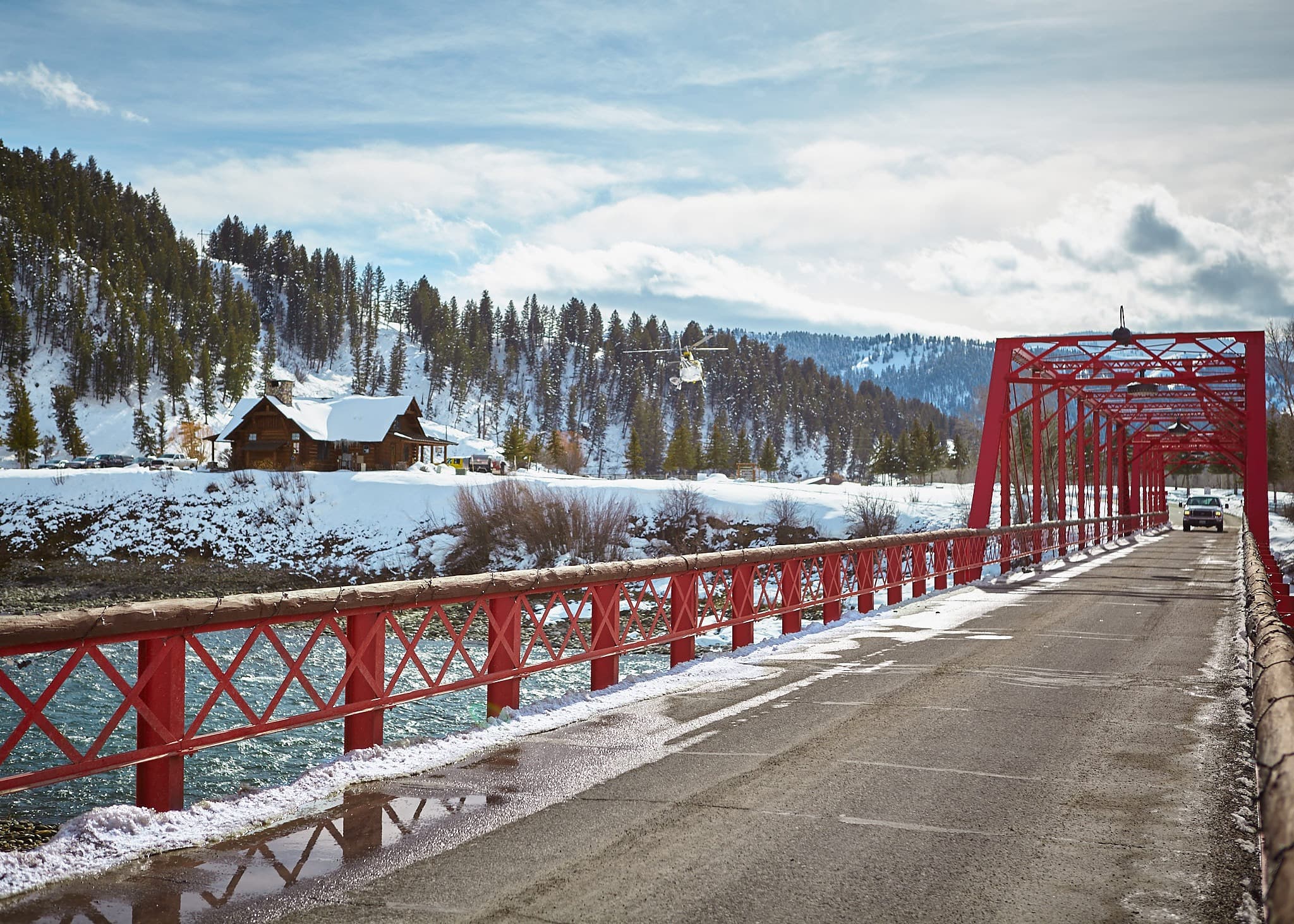 Historic red bridge over the Snake River with a helicopter overhead in winter at Snake River Sporting Club in Jackson Hole, Wyoming