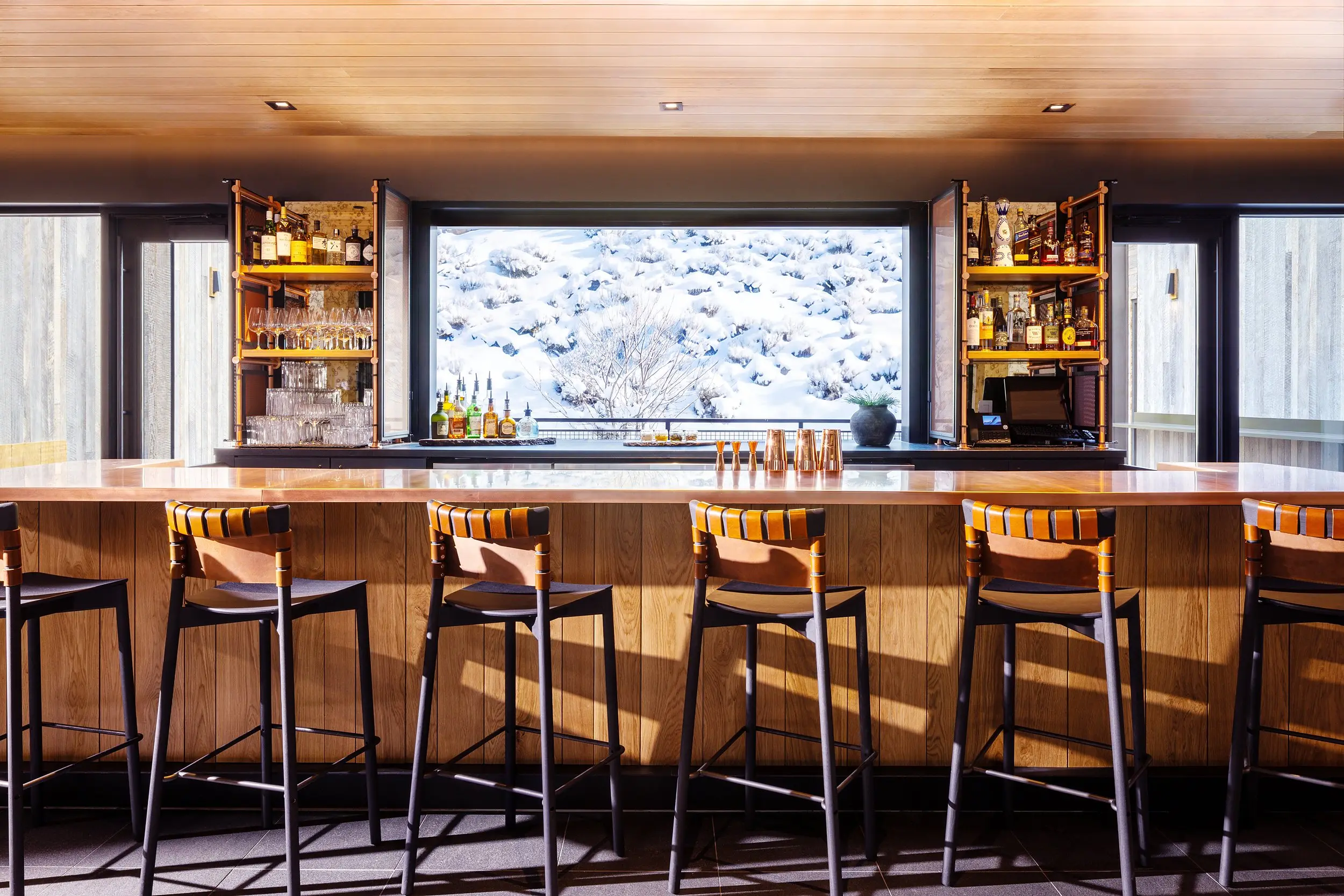 Dark Sky Bar at Snake River Sporting Club in Jackson Hole, Wyoming, with leather-strap barstools, a copper bar top, and a window framing snowy sagebrush.