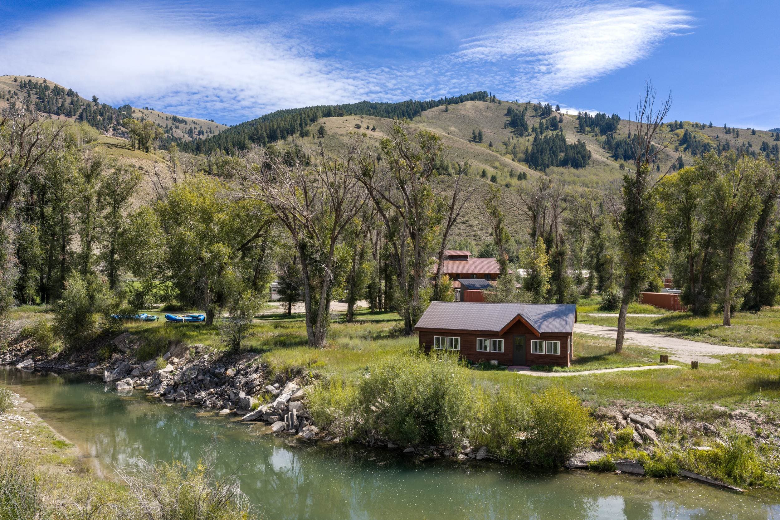 Rustic fishing cabin along the river with cottonwoods and mountains at Snake River Sporting Club in Jackson Hole, Wyoming